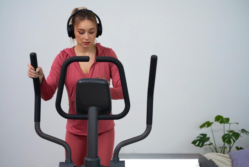 Девушка в наушниках занимается на эллипсе