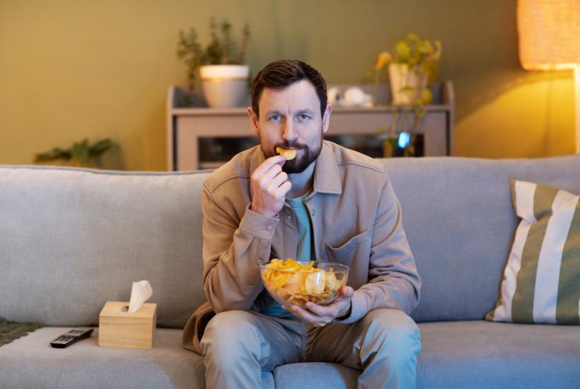 Человек смотрит телевизор и ест чипсы